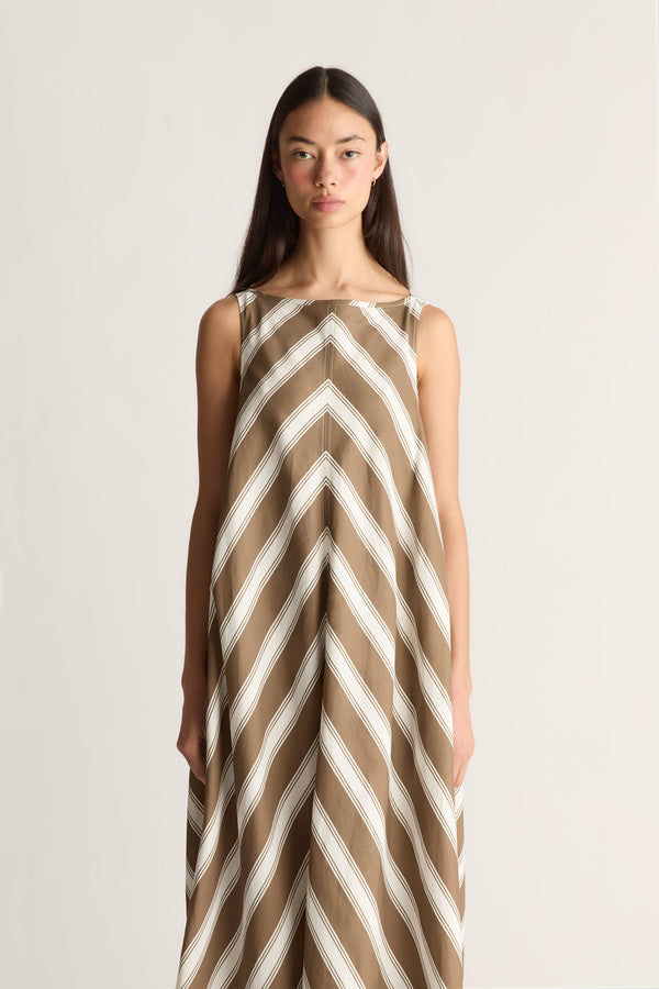 A woman modeling a sleeveless maxi dress with a brown and off-white chevron pattern against a plain light background.
