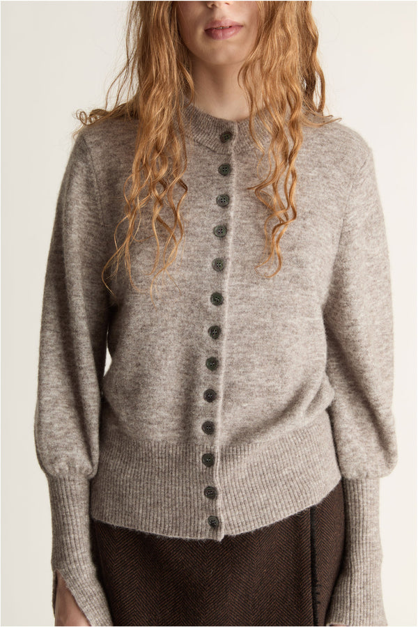 Woman wearing a gray sweater and brown skirt on a plain background