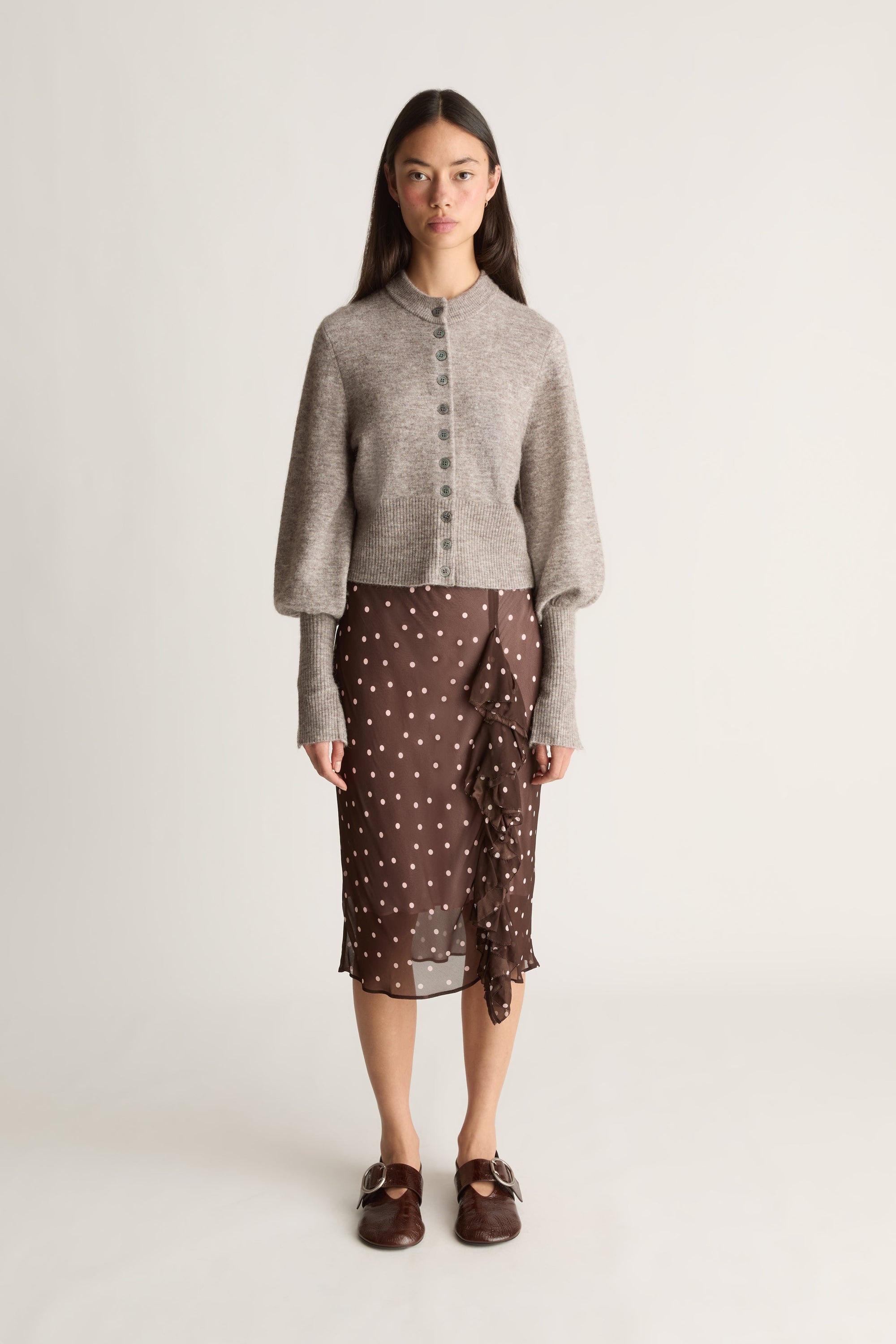 Front view of a woman wearing a gray cardigan and brown polka dot skirt on a white background