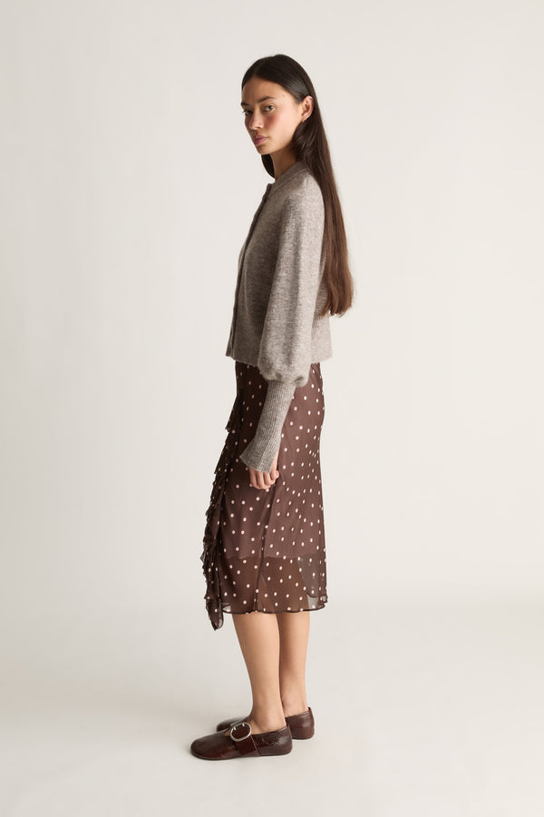 Side view of a woman wearing a brown polka dot skirt  and gray sweater on a white background