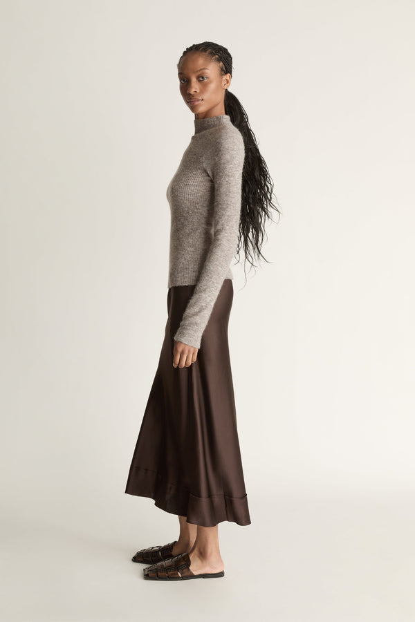 Woman wearing a gray turtleneck sweater and brown skirt against a beige background